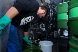 Mitarbeiter Felix befüllt mit einem Schlauch Bierfässer im Kühlraum. Foto: Holger Vogel